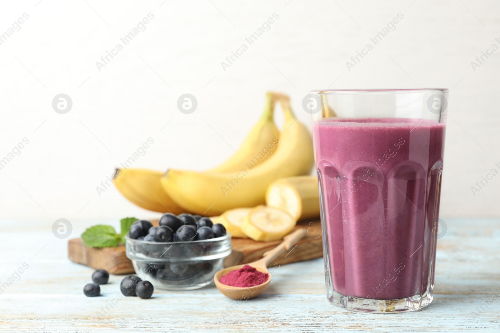 Photo of Fresh acai drink with berries and bananas on wooden table against light background