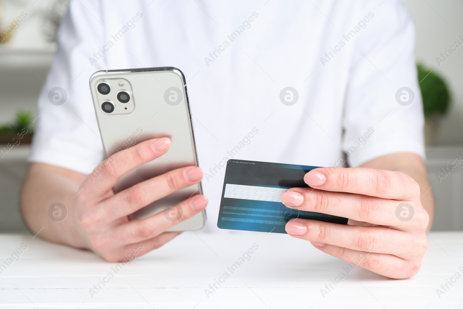 Photo of Online payment. Woman with smartphone and credit card at white table, closeup