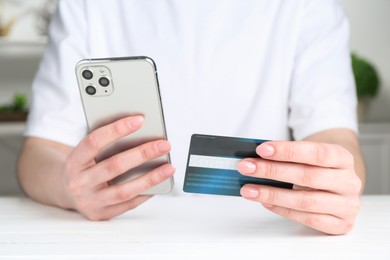 Online payment. Woman with smartphone and credit card at white table, closeup