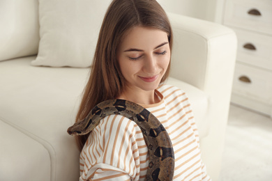 Photo of Young woman with boa constrictor at home. Exotic pet