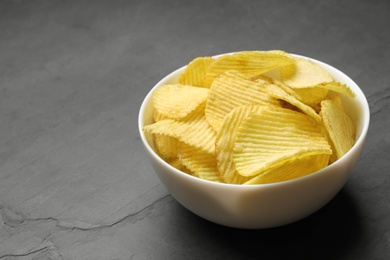 Photo of Bowl of potato chips on grey table. Space for text