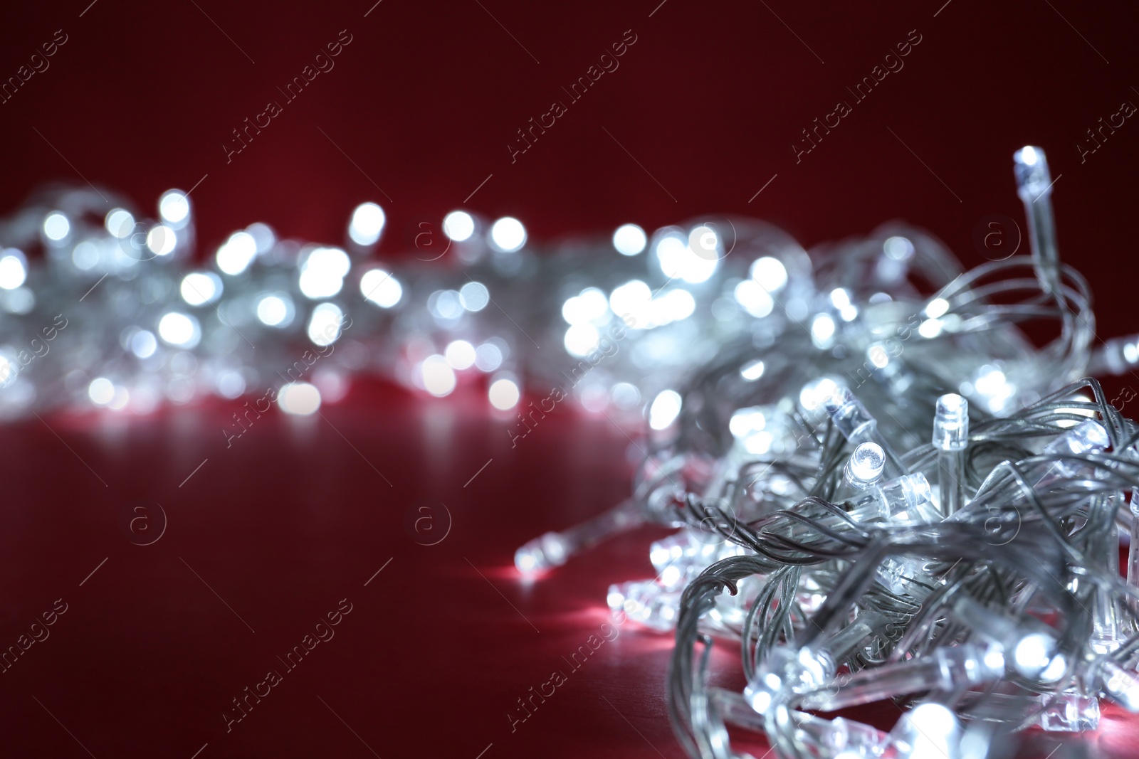 Photo of Glowing Christmas lights on burgundy background, closeup . Space for text