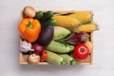 Crate with different fresh vegetables on light background, top view