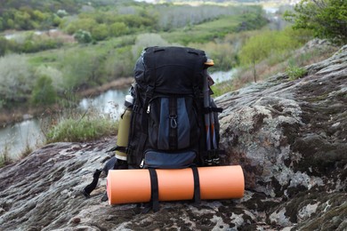 Photo of Backpack with camping mat and trekking poles on rocky hill