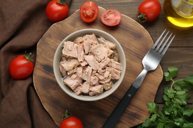 Bowl with canned tuna and products on wooden table, flat lay