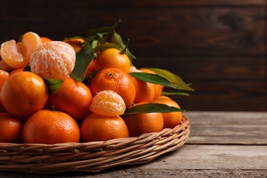 Photo of Fresh ripe juicy tangerines and green leaves on wooden table, closeup with space for text