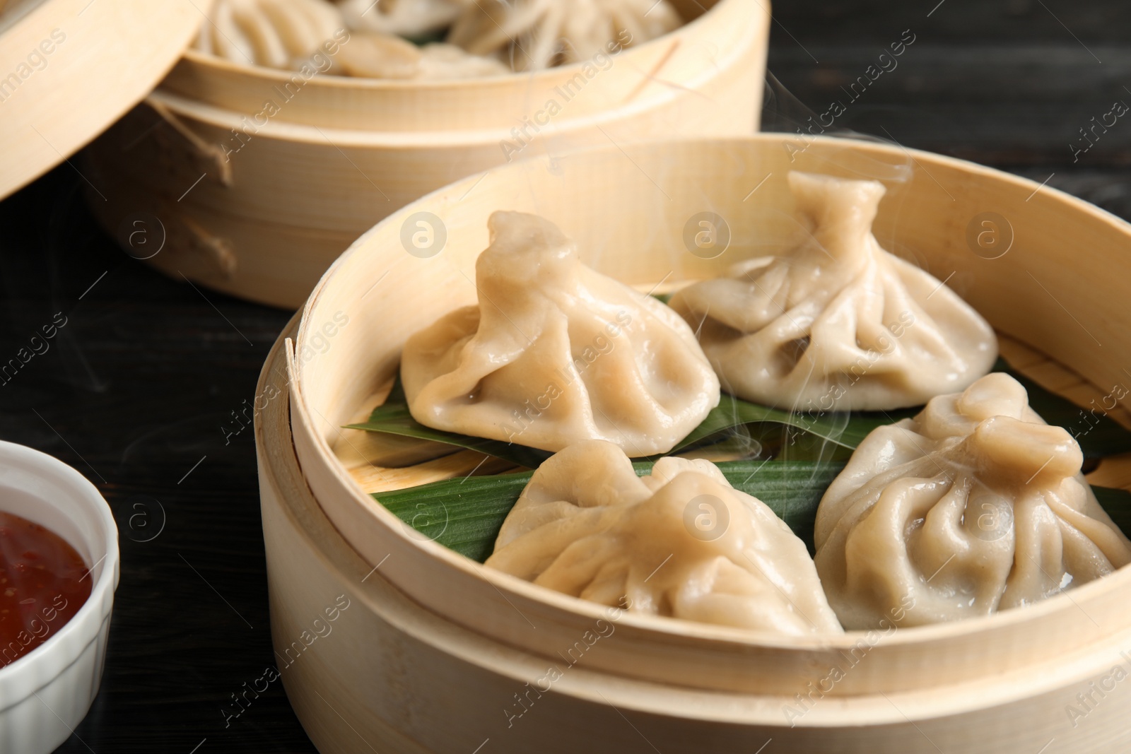 Photo of Bamboo steamers with tasty baozi dumplings and bowl of sauce on table