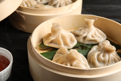 Photo of Bamboo steamers with tasty baozi dumplings and bowl of sauce on table