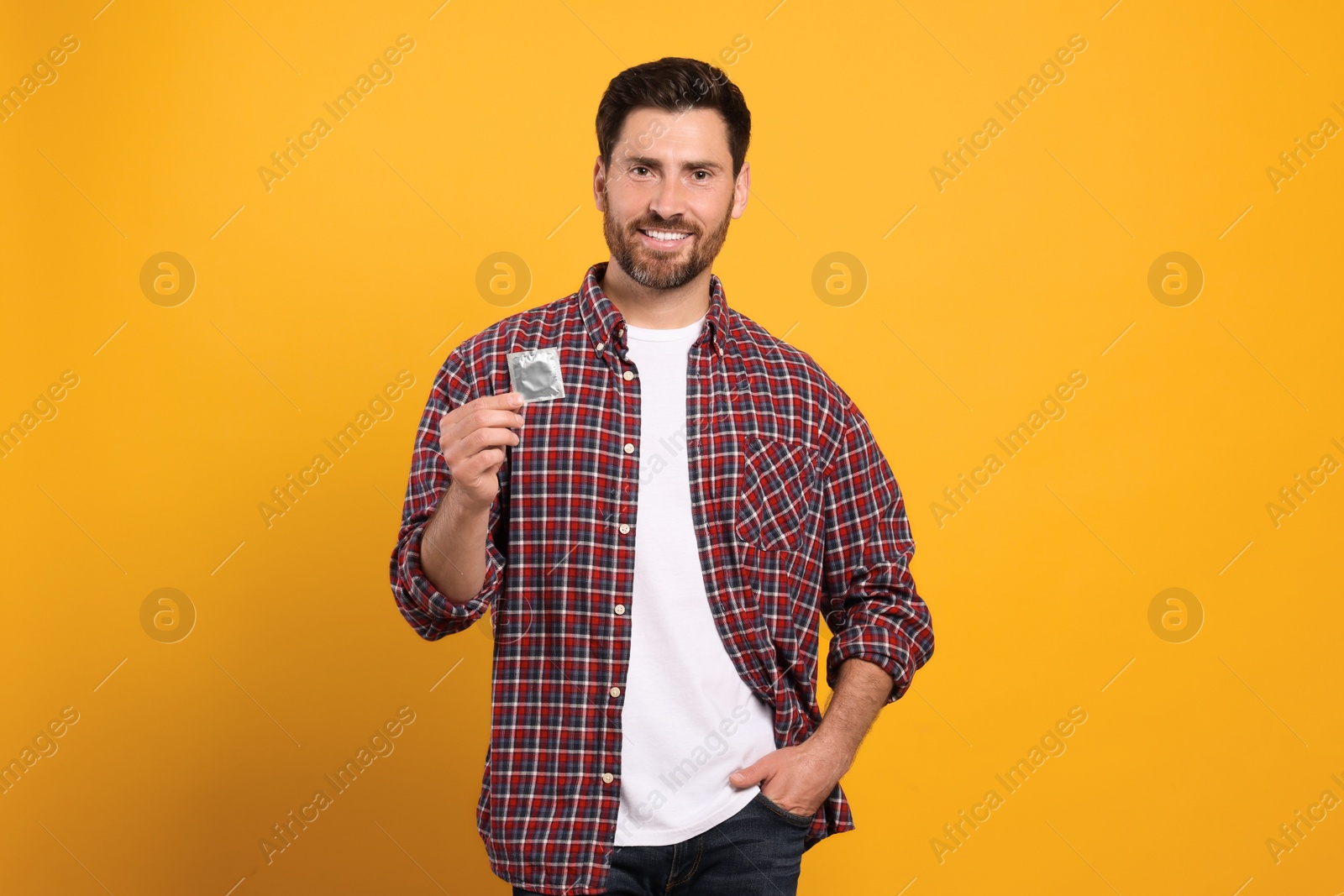 Photo of Happy man holding condom on yellow background, space for text. Safe sex