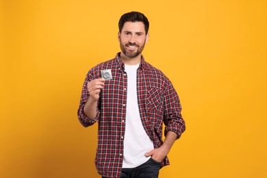 Happy man holding condom on yellow background, space for text. Safe sex