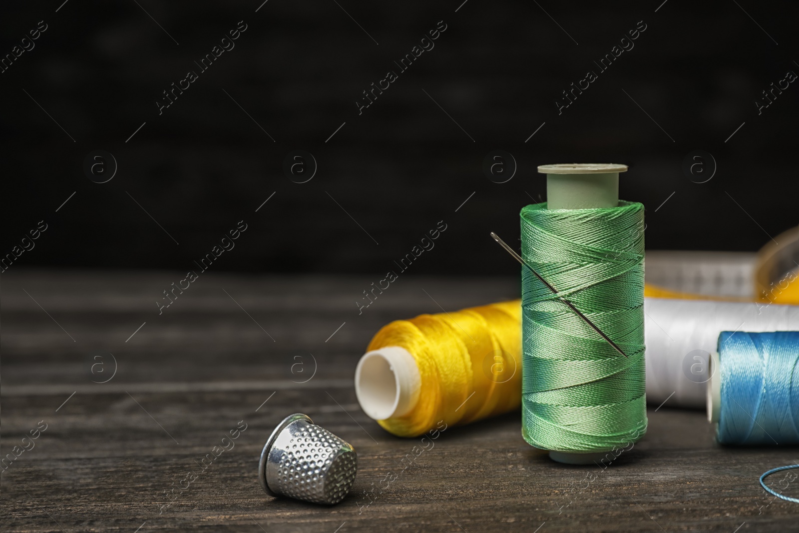 Photo of Color sewing threads, needle and thimble on wooden table