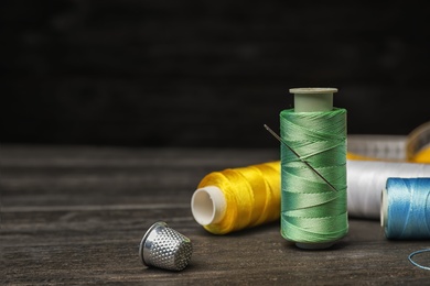 Photo of Color sewing threads, needle and thimble on wooden table