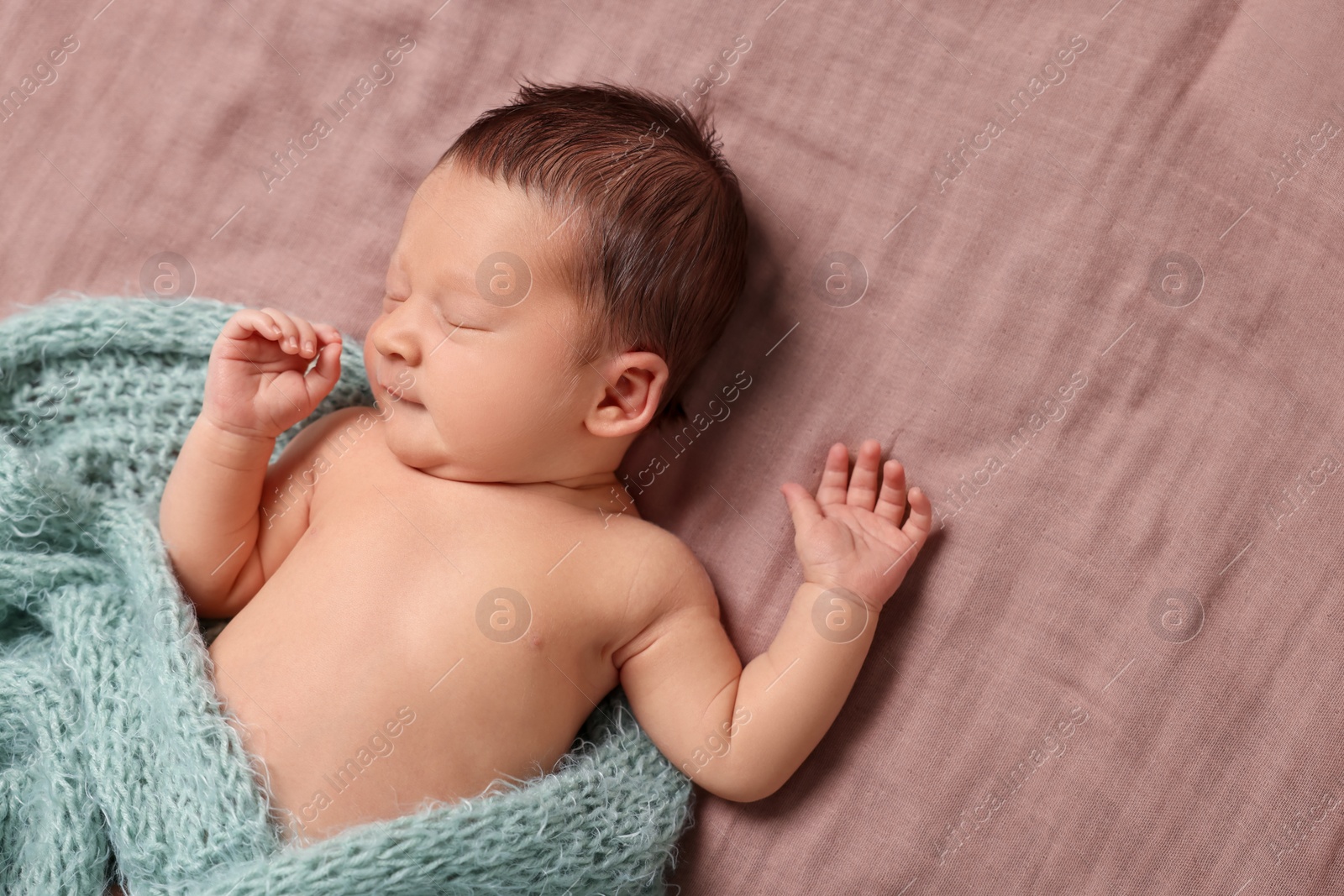 Photo of Adorable newborn baby in turquoise knitted blanket sleeping on bed, top view. Space for text