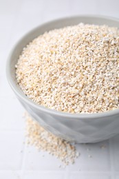 Photo of Dry barley groats in bowl on white tiled table, closeup