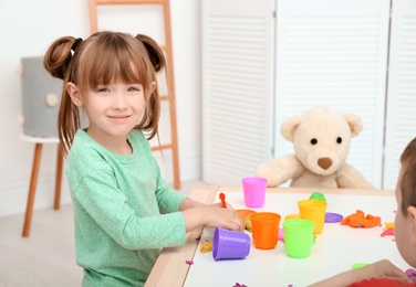 Cute little girl using play dough at table indoors