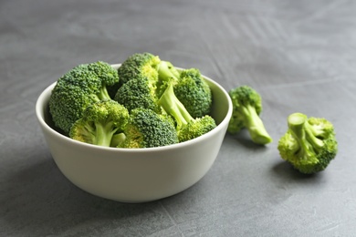 Photo of Bowl and fresh broccoli on grey table. Space for text