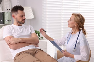 Photo of Doctor with clipboard consulting patient in clinic