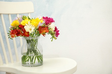 Photo of Beautiful spring freesia flowers in vase on chair. Space for text