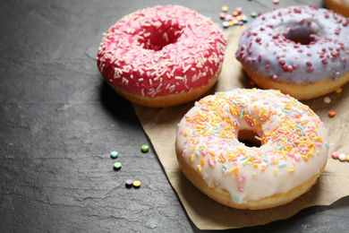 Photo of Yummy donuts with sprinkles on dark background, closeup