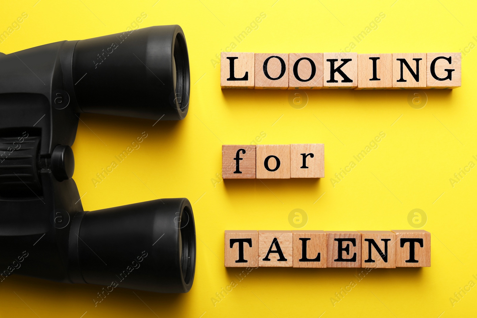 Photo of Staff recruitment concept. Phrase Looking For Talent made of wooden cubes and binoculars on yellow background, flat lay