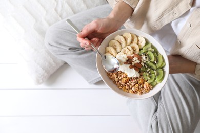 Photo of Woman eating tasty granola indoors, top view