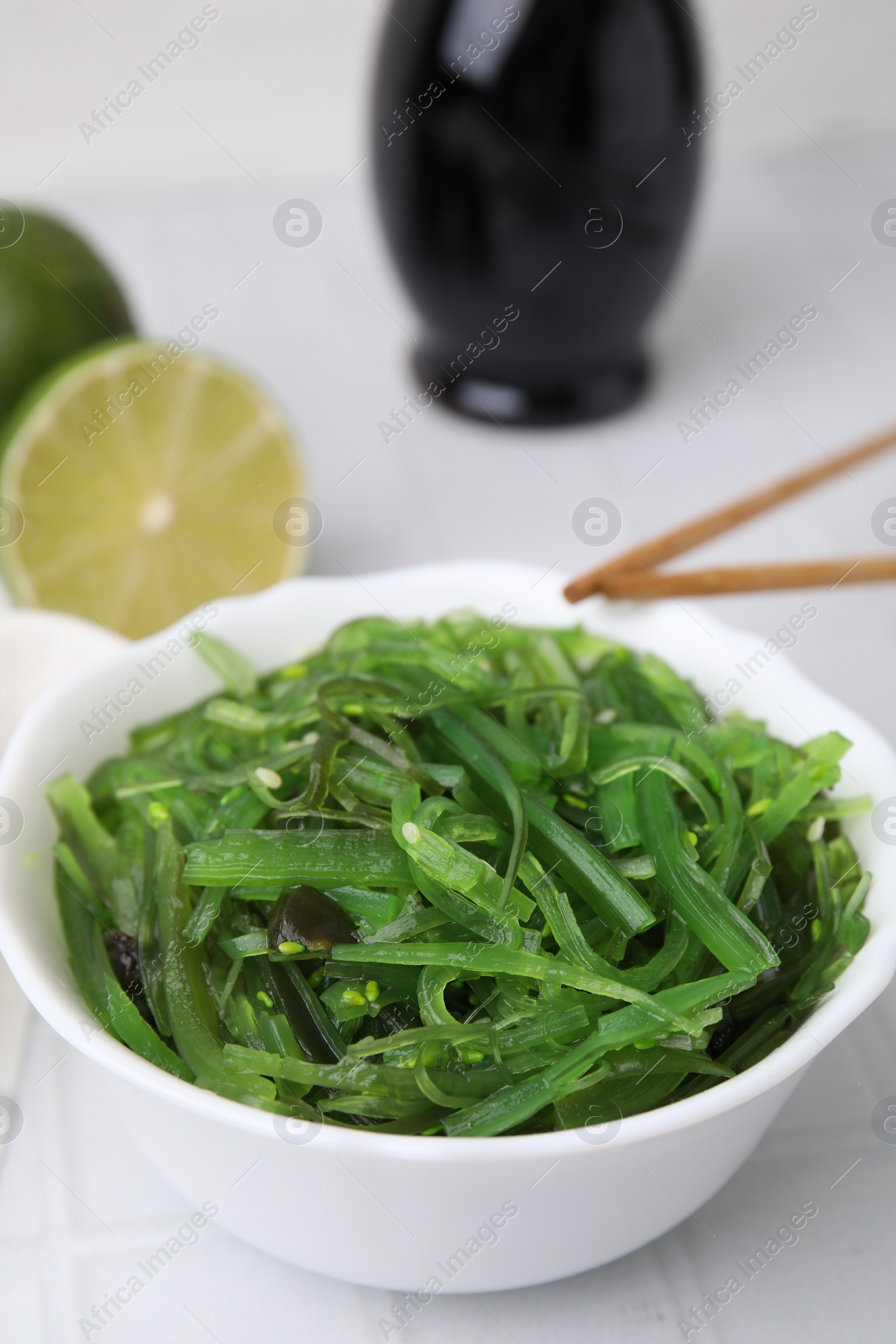 Photo of Tasty seaweed salad in bowl on white tiled table, closeup