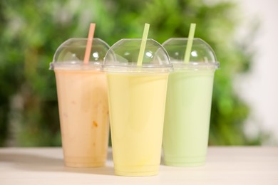 Photo of Plastic cups with different tasty smoothies on wooden table outdoors