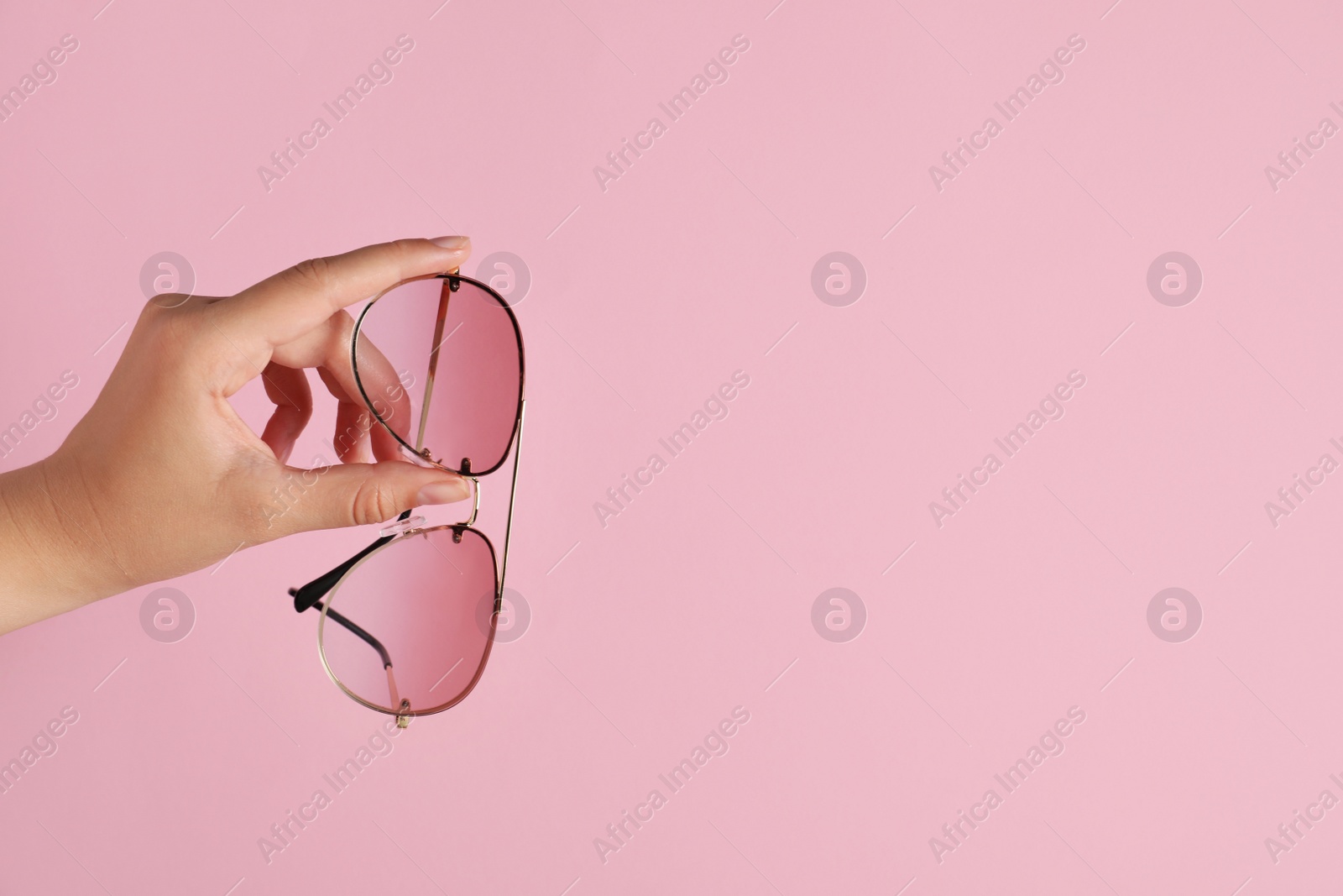 Photo of Woman holding stylish sunglasses on pink background, closeup of hand. Space for text