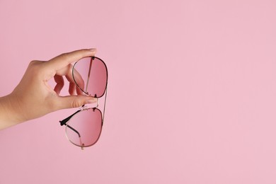 Photo of Woman holding stylish sunglasses on pink background, closeup of hand. Space for text