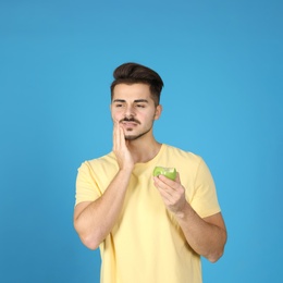 Photo of Emotional young man with sensitive teeth and apple on color background