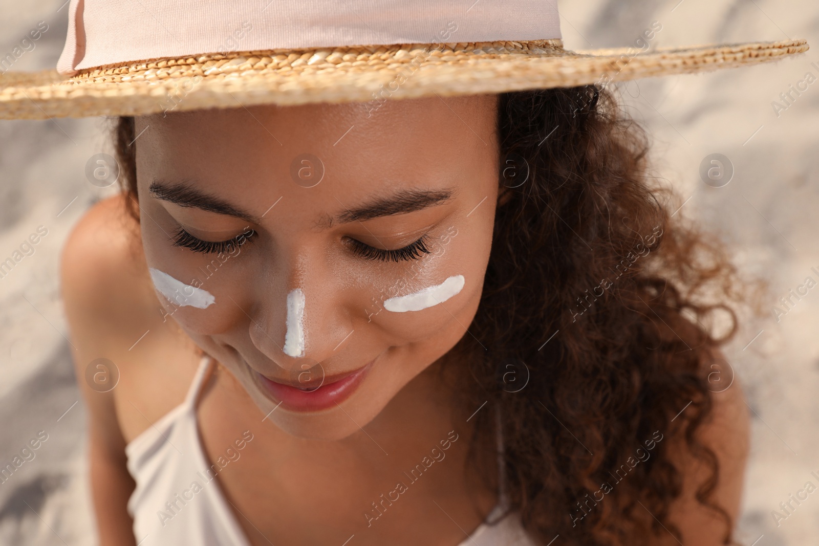 Photo of Beautiful African American woman with sun protection cream on face at sandy beach, closeup