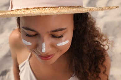 Photo of Beautiful African American woman with sun protection cream on face at sandy beach, closeup