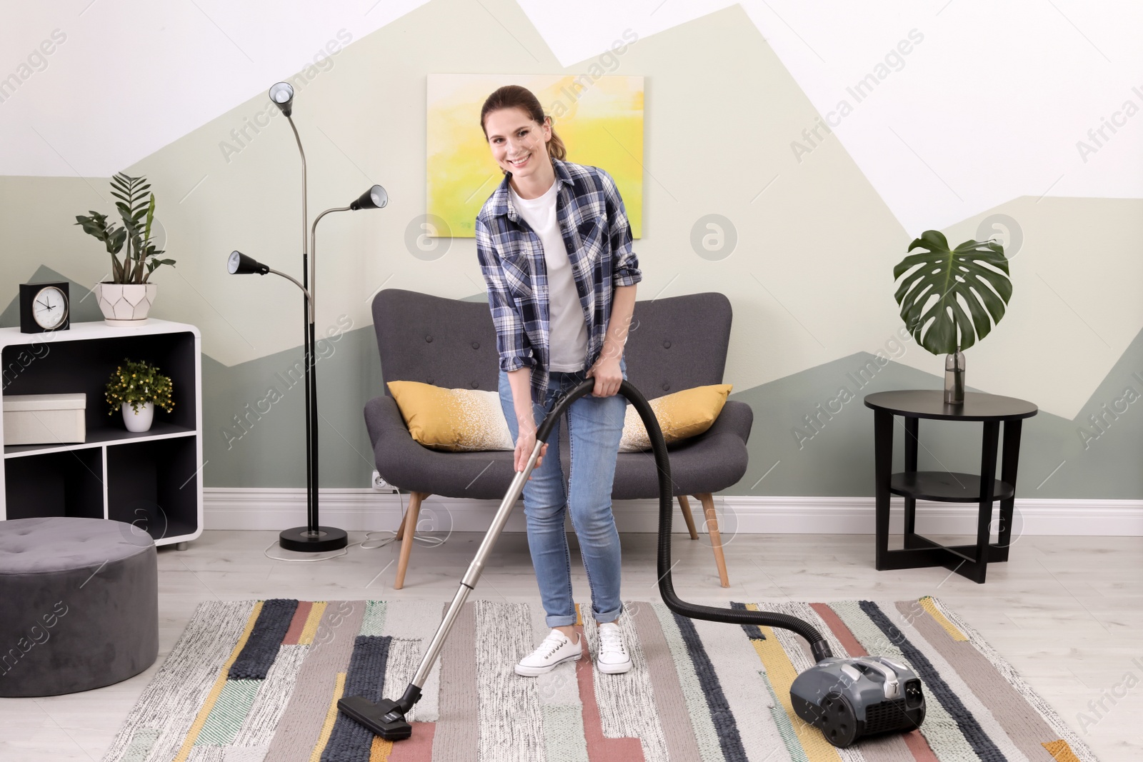 Photo of Woman removing dirt from carpet with vacuum cleaner at home