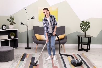 Woman removing dirt from carpet with vacuum cleaner at home