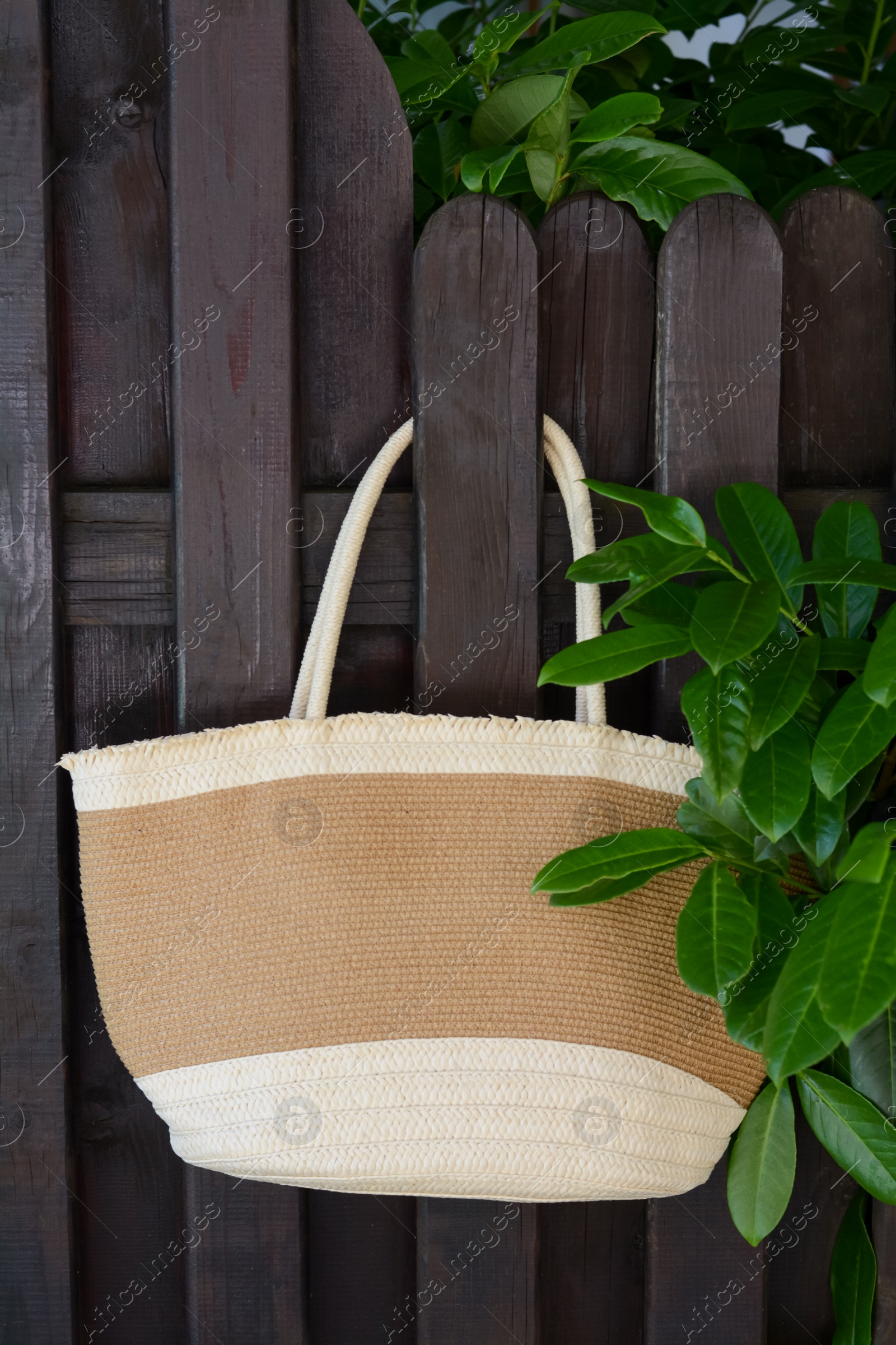 Photo of Stylish bag hanging on wooden fence outdoors. Beach accessory