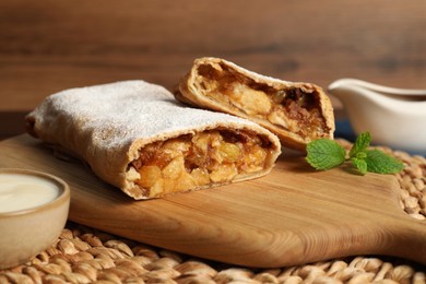 Photo of Delicious strudel with apples, nuts and raisins on wicker mat, closeup