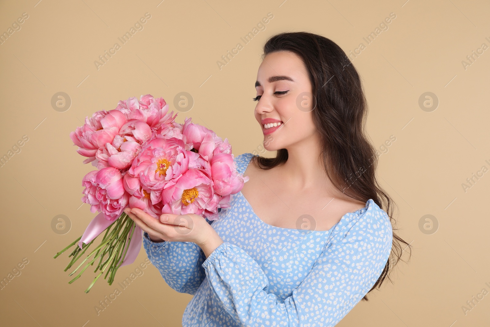 Photo of Beautiful young woman with bouquet of pink peonies on beige background