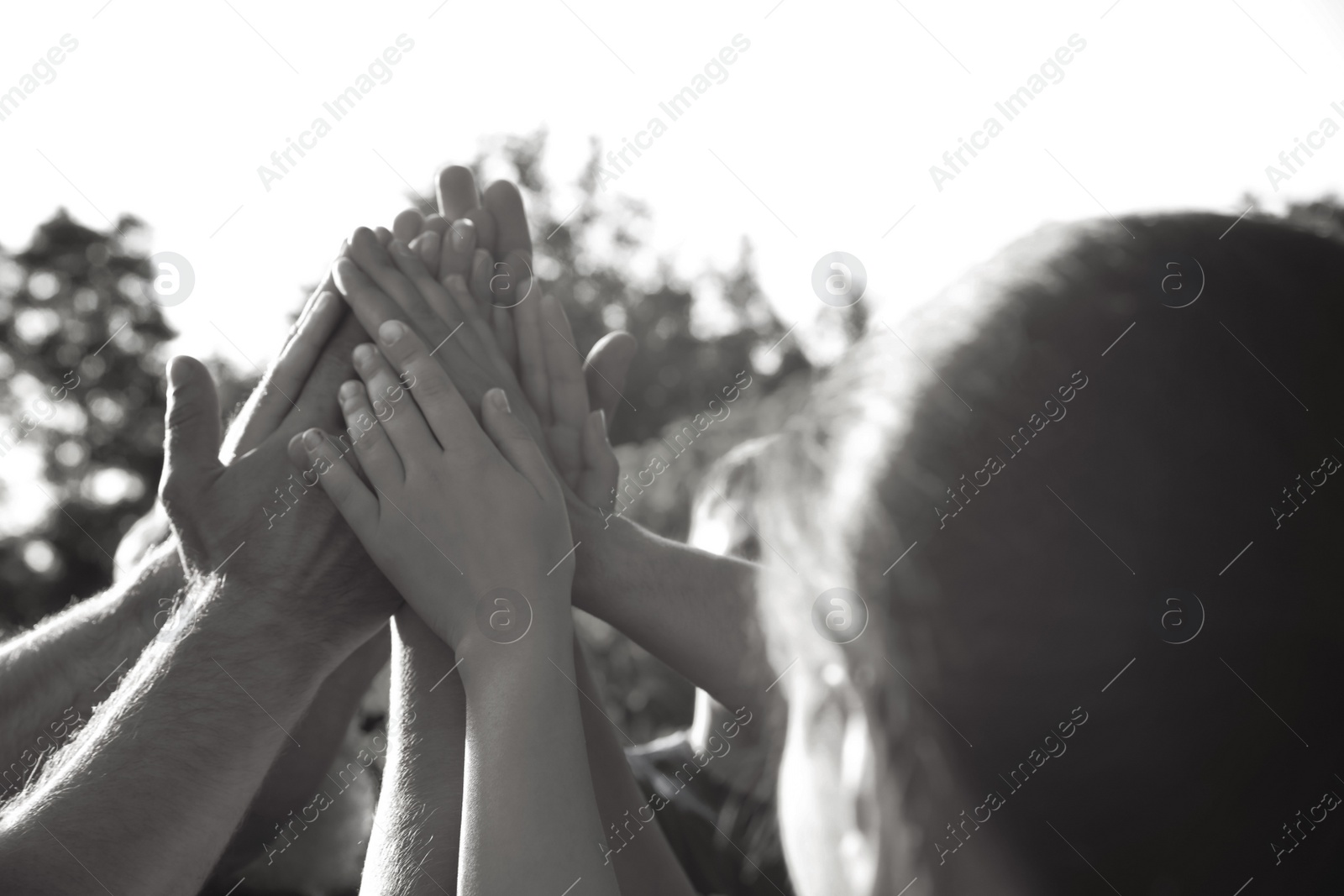 Image of Group of volunteers joining hands together outdoors. Black and white effect