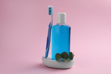 Fresh mouthwash in bottle and toothbrush on pink background, closeup