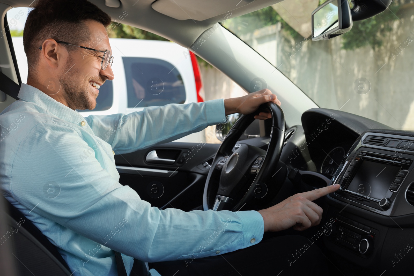 Photo of Listening to radio while driving. Handsome man turning volume button on vehicle audio in car