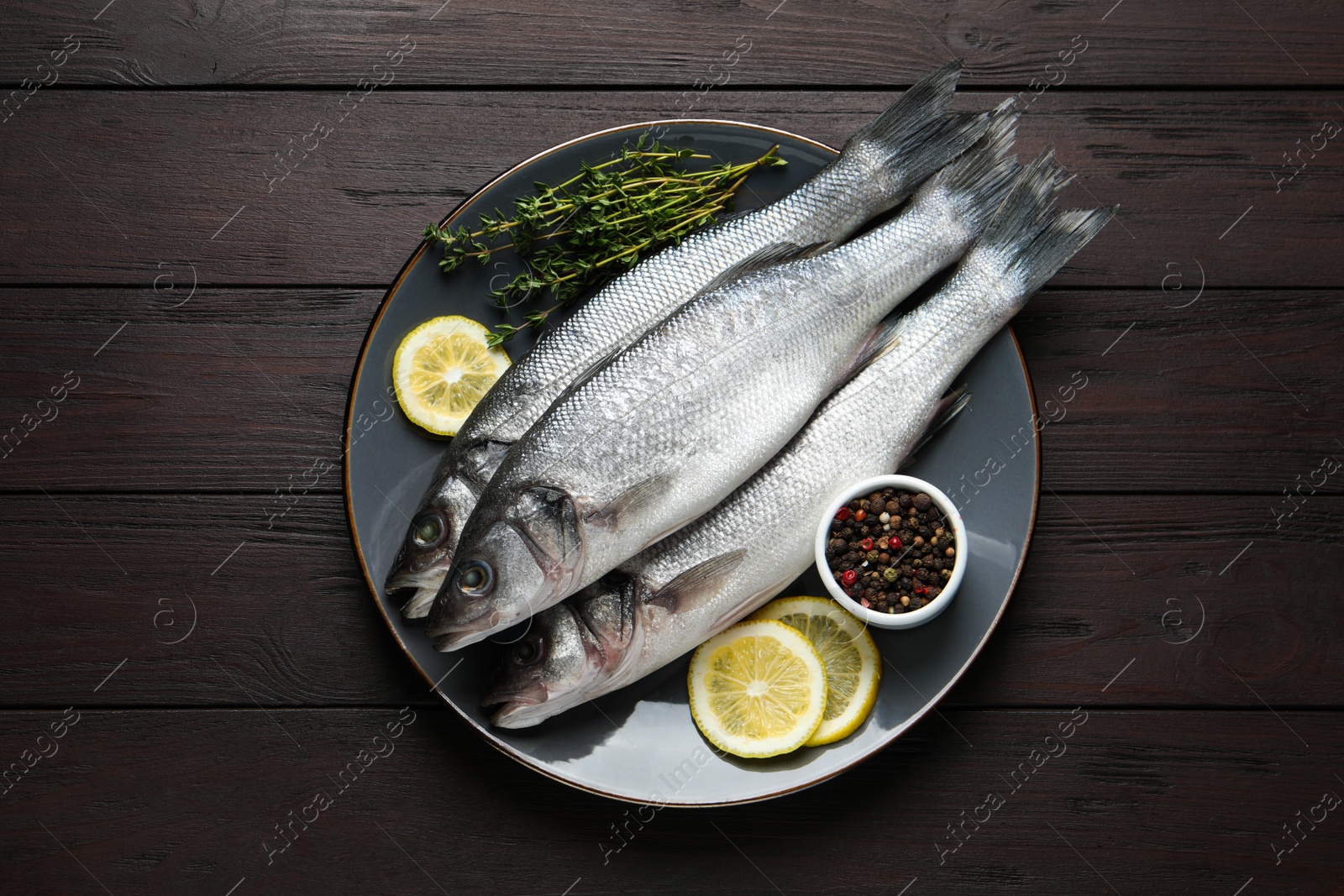 Photo of Tasty sea bass fish with spices on dark wooden table, top view