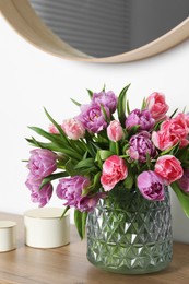 Photo of Beautiful bouquet of colorful tulip flowers on wooden chest of drawers near white wall