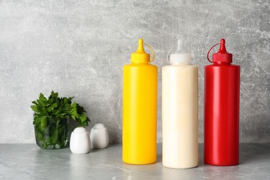 Photo of Bottles of mustard, ketchup and mayonnaise on light grey table