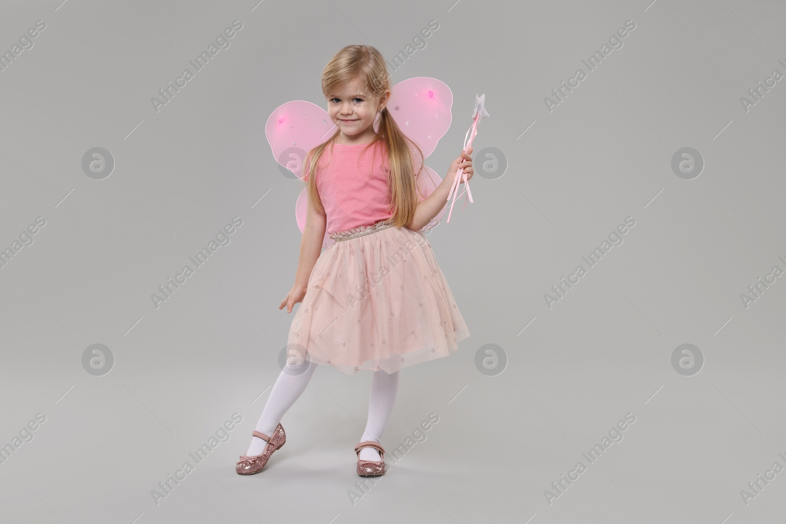 Photo of Cute little girl in fairy costume with pink wings and magic wand on light grey background