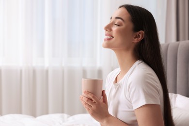 Photo of Happy woman with cup of drink at home, space for text. Lazy morning