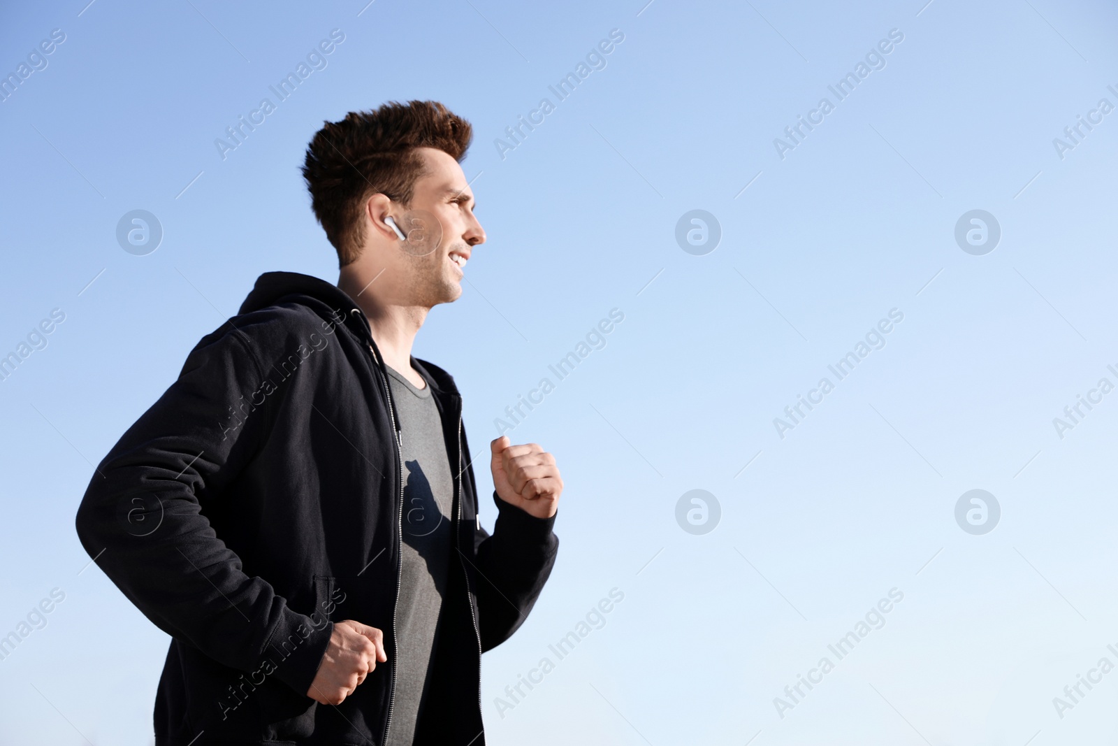 Photo of Young sportsman with wireless earphones running outdoors