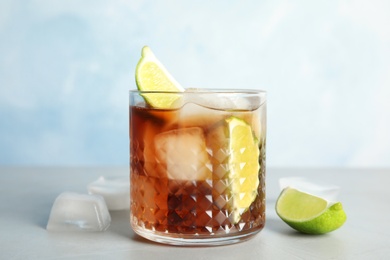 Glass of cocktail with cola, ice and cut lime on table