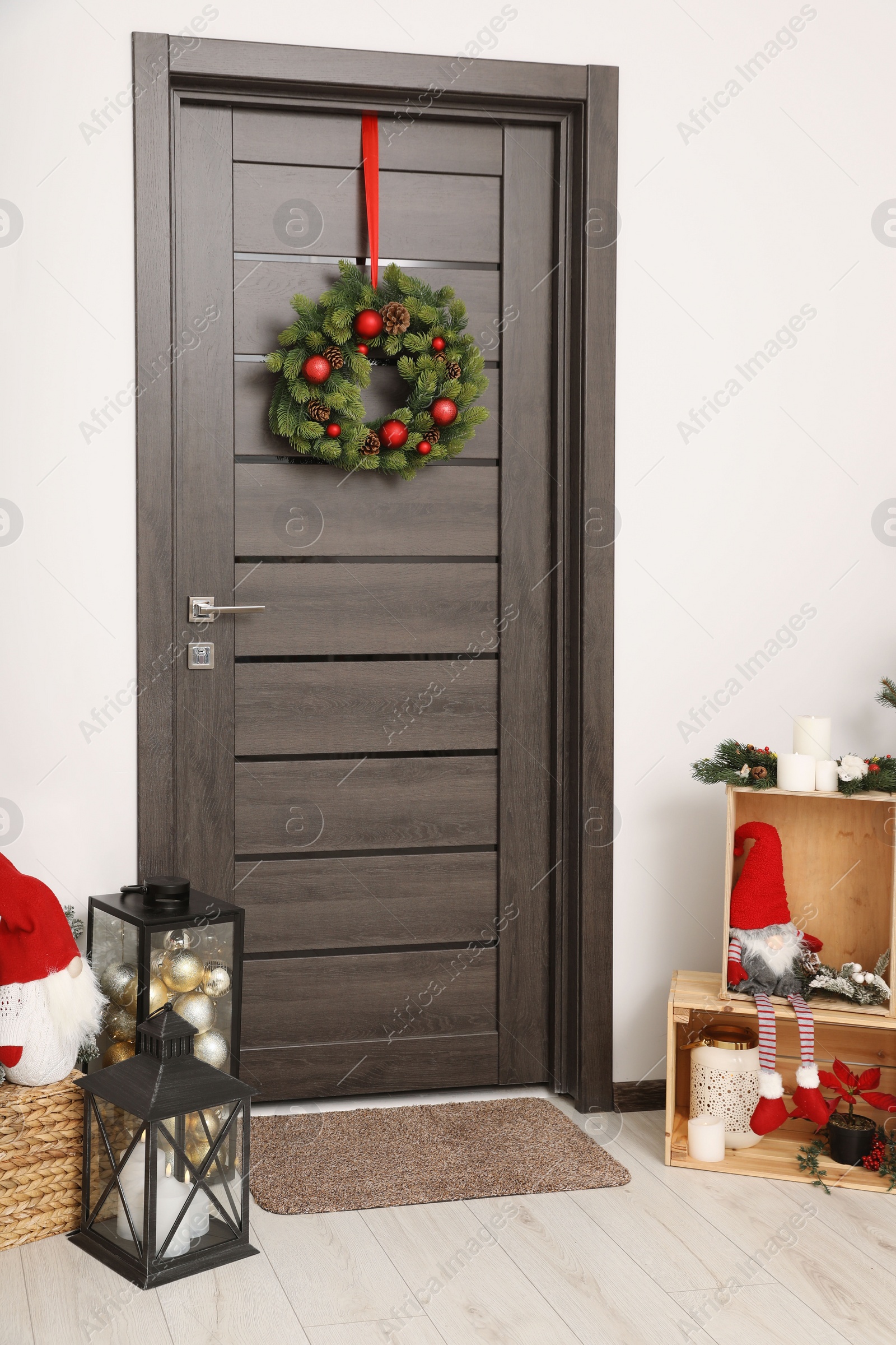 Photo of Christmas wreath hanging on wooden door and festive decoration indoors