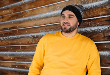 Young man wearing warm clothes near wooden wall.  Winter vacation
