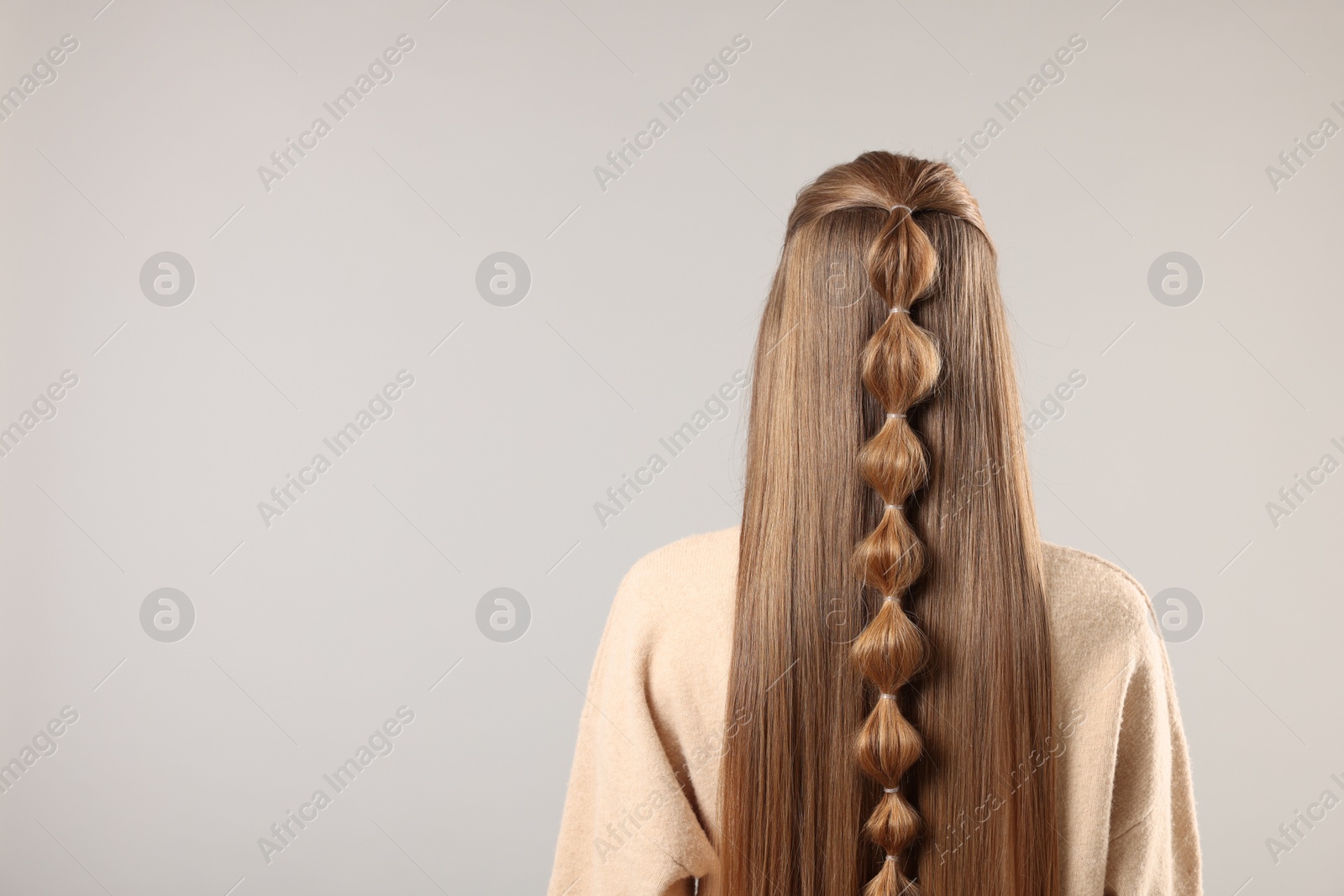 Photo of Woman with braided hair on grey background, back view. Space for text